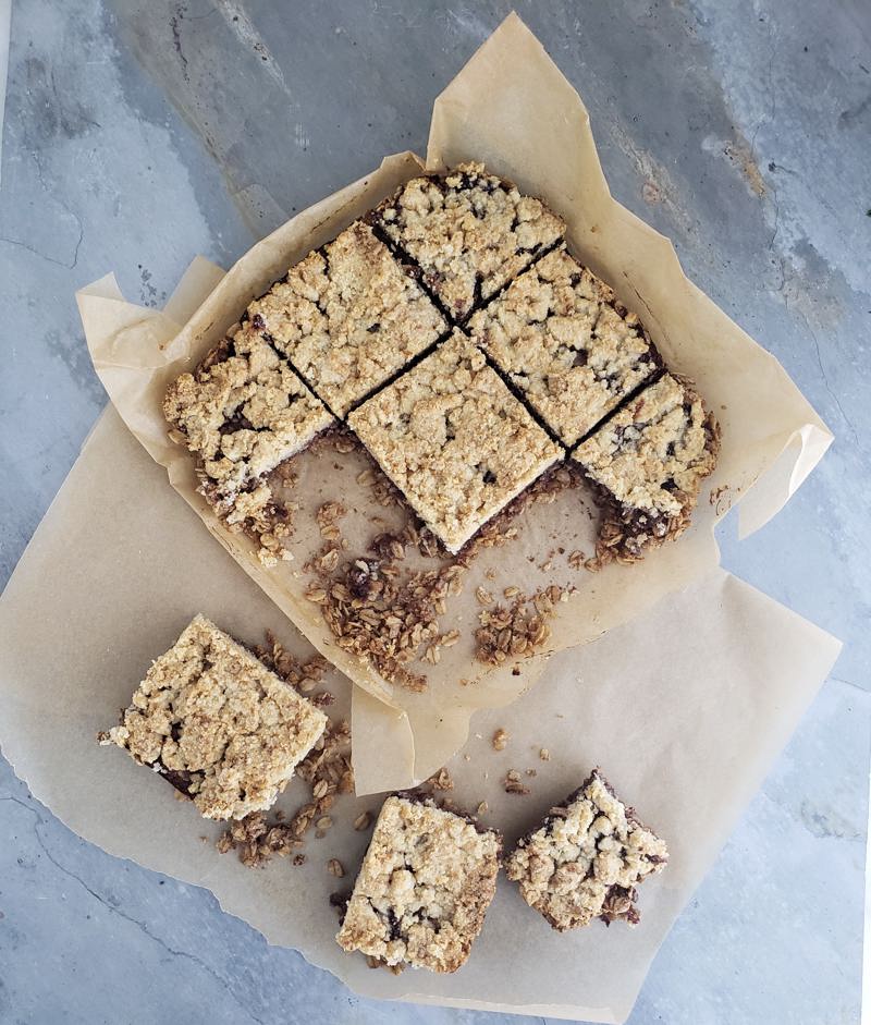 A dish of oatmeal bars with three crumbly squares removed, sitting on parchment paper.