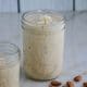 Coconut almond smoothie in a ball jar on a marble table with coconut flakes and almonds in the background with lots of sunlight coming in the window.