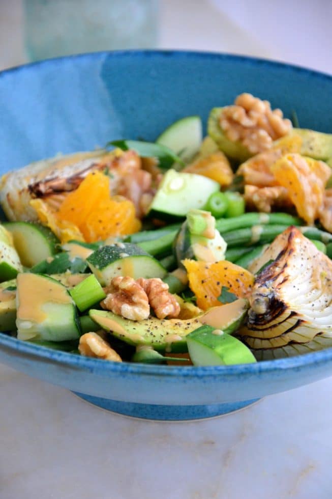 This French Green Bean Salad is ideal for lunch filled with avocado, oranges, walnuts, roasted onions and more in a deep blue bowl.